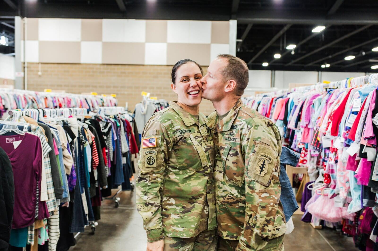 A military husband in camo kisses his military wife, also in camo.