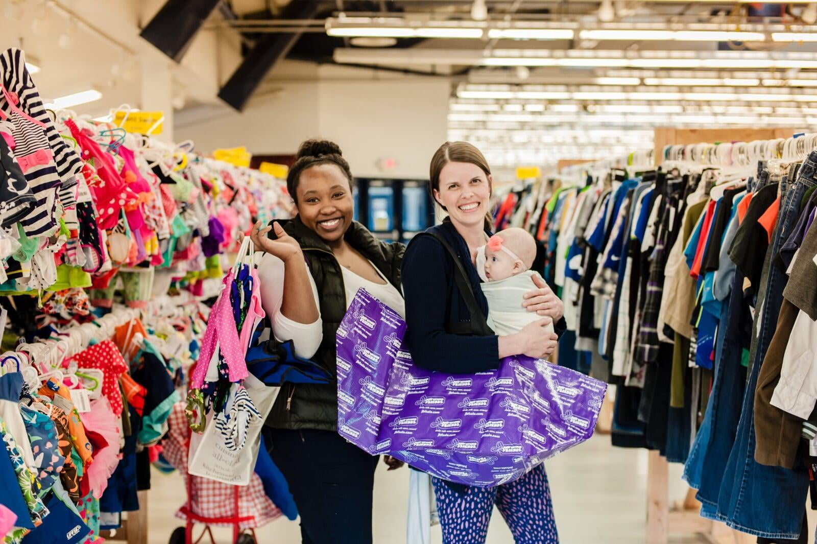 Two friends shop together—one mom wears her baby girl—as they find great deals at the JBF sale.