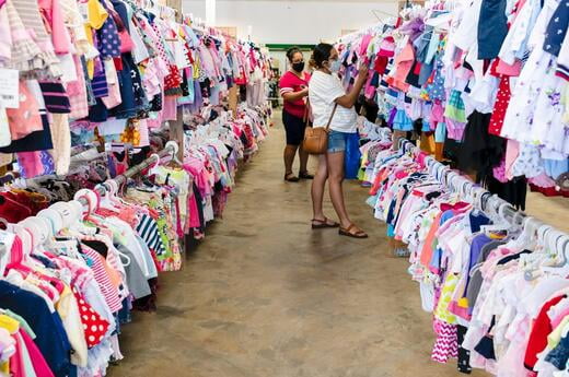 Shoppers looking at clothing hanging on clothing racks. The shoppers are in an aisle between the clothing racks.